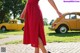 A woman in a red dress standing in front of a yellow car.