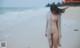 A naked woman standing on a beach next to the ocean.