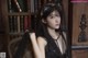 A woman in a black dress sitting in front of a bookcase.