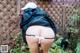 A woman in a black jacket and white thong is bending over in the garden.