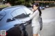 A woman standing next to a black car talking on a cell phone.