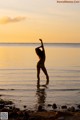 A woman in a bikini standing in the water at sunset.