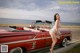 A woman leaning on the hood of a red convertible car.