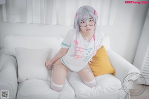 A woman sitting on a white couch wearing glasses.