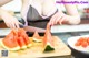 A woman cutting up a slice of watermelon on a cutting board.